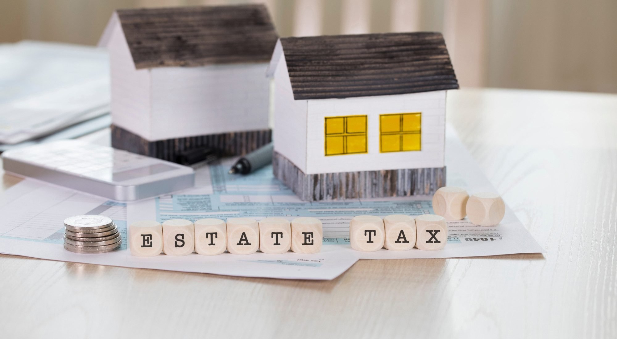 A photo of two paper houses sitting on a table with wooden blocks spelling "Estate Tax" in front of them.